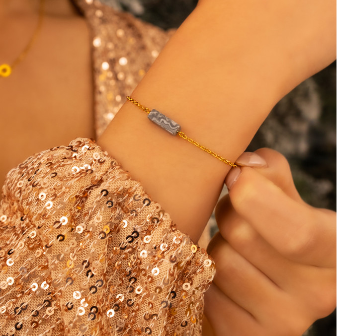 Model draagt gouden armband met grijs steentje