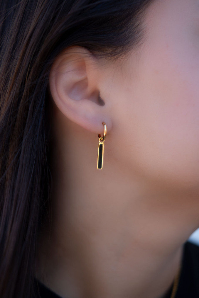 Het model draagt de goudkleurige bar oorbellen met zwart hangertje in haar oor