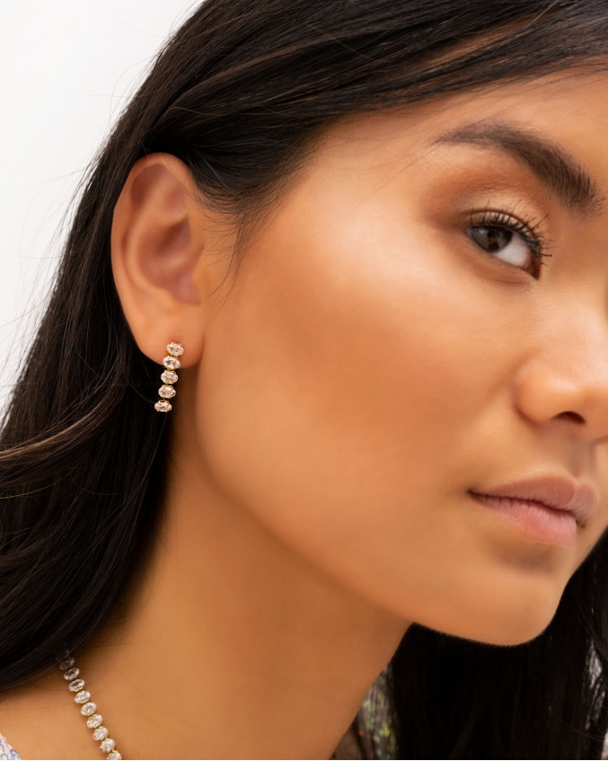 Model draagt gouden tennis oorbellen met ovale steentjes