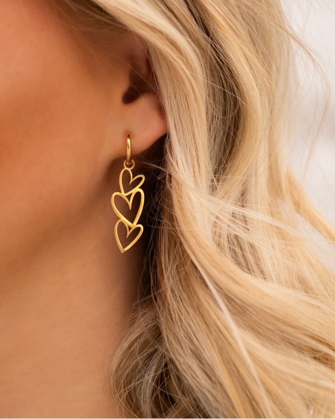 Model draagt gouden oorbellen met hartjes