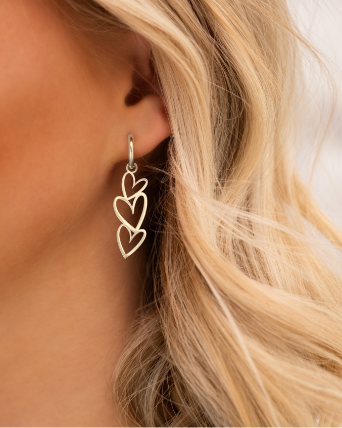 Model draagt zilveren oorbellen triple heart