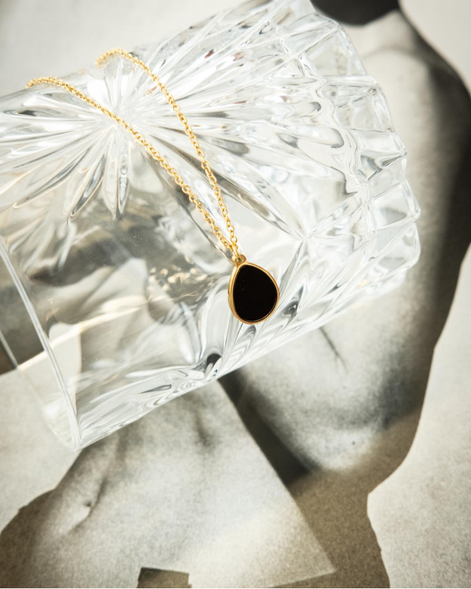 De goudkleurige druppel ketting zwart ligt op een kristallen glas