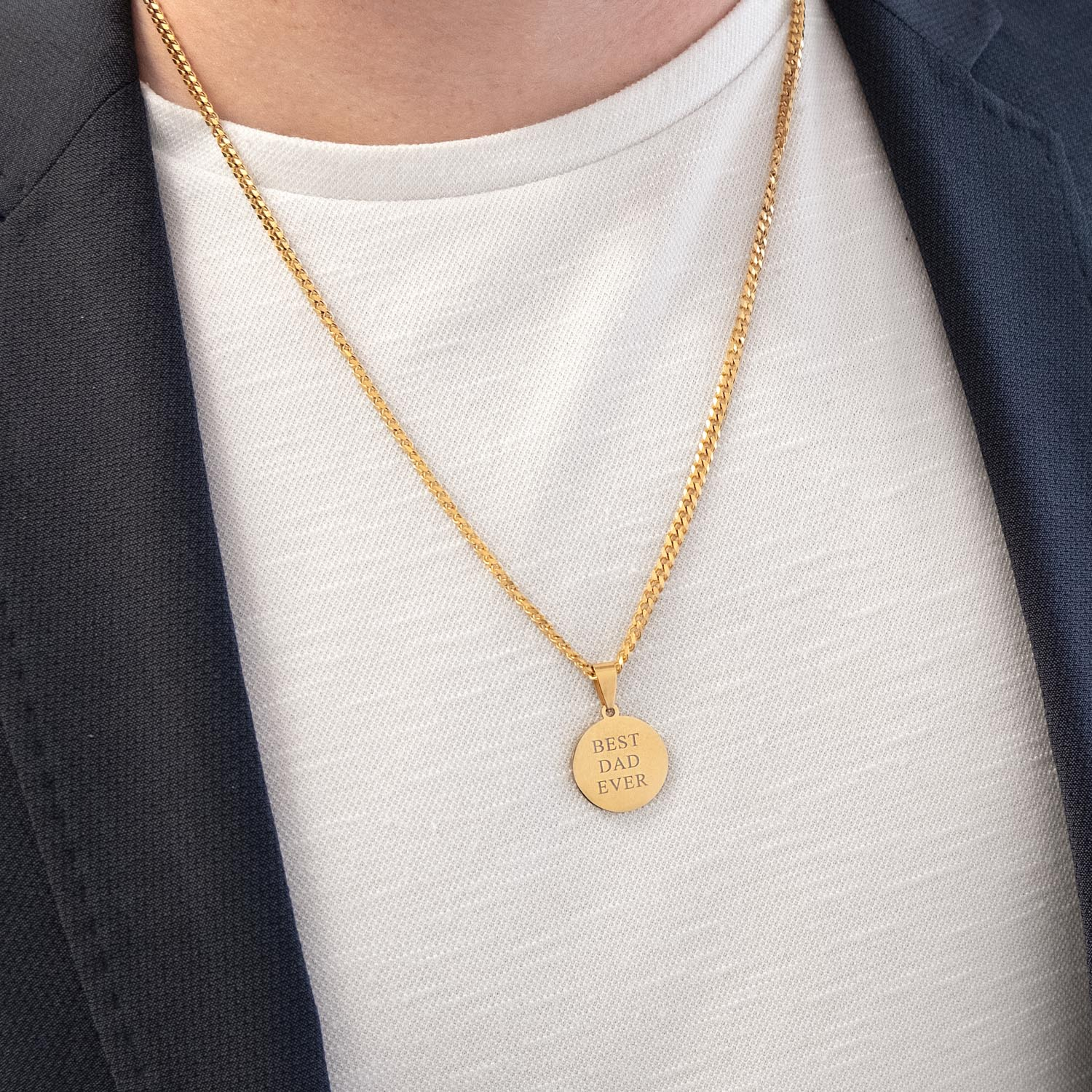 Man draagt een gouden ronde ketting met gravering om de hals