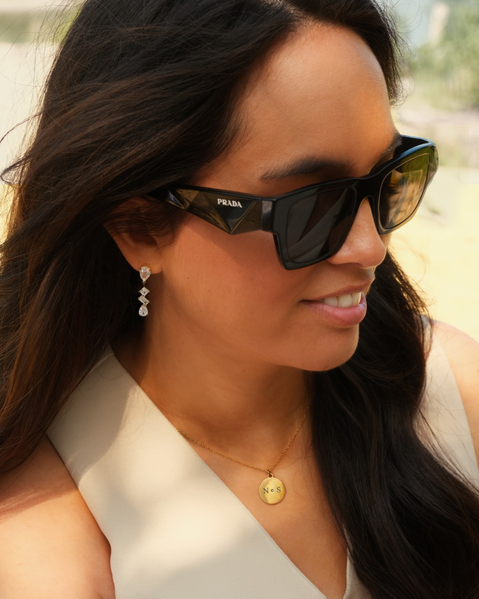 gouden sparkle oorbellen gecombineerd met initial ketting bij vrouw met zonnebril