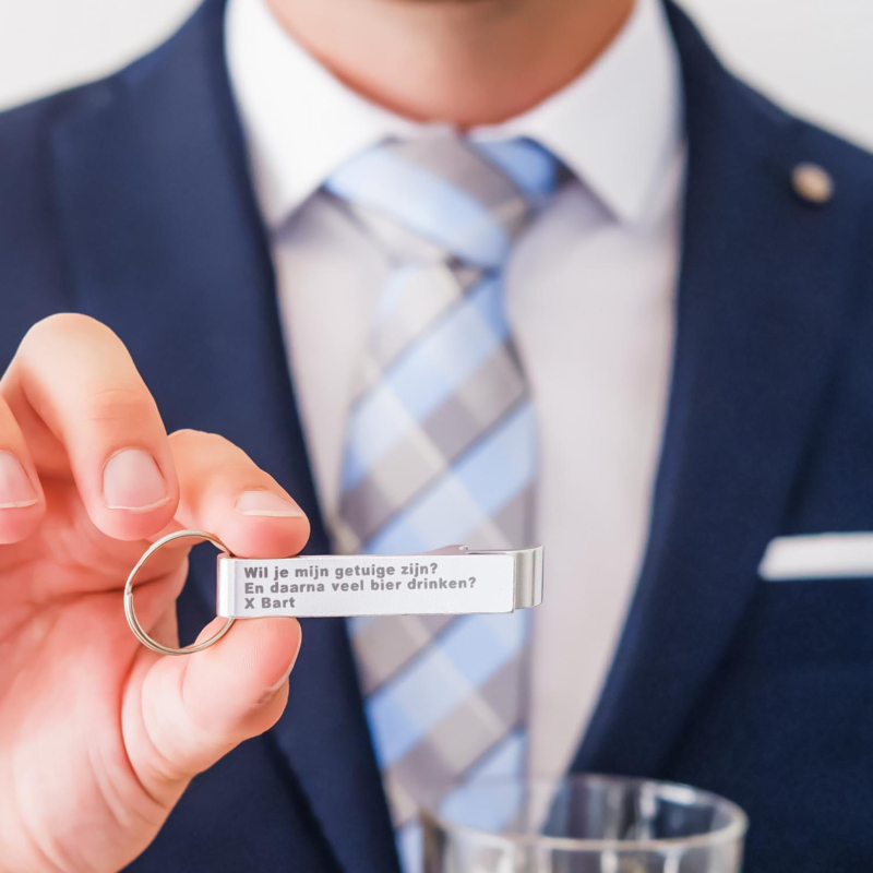Zilveren bieropener in de hand met gravering