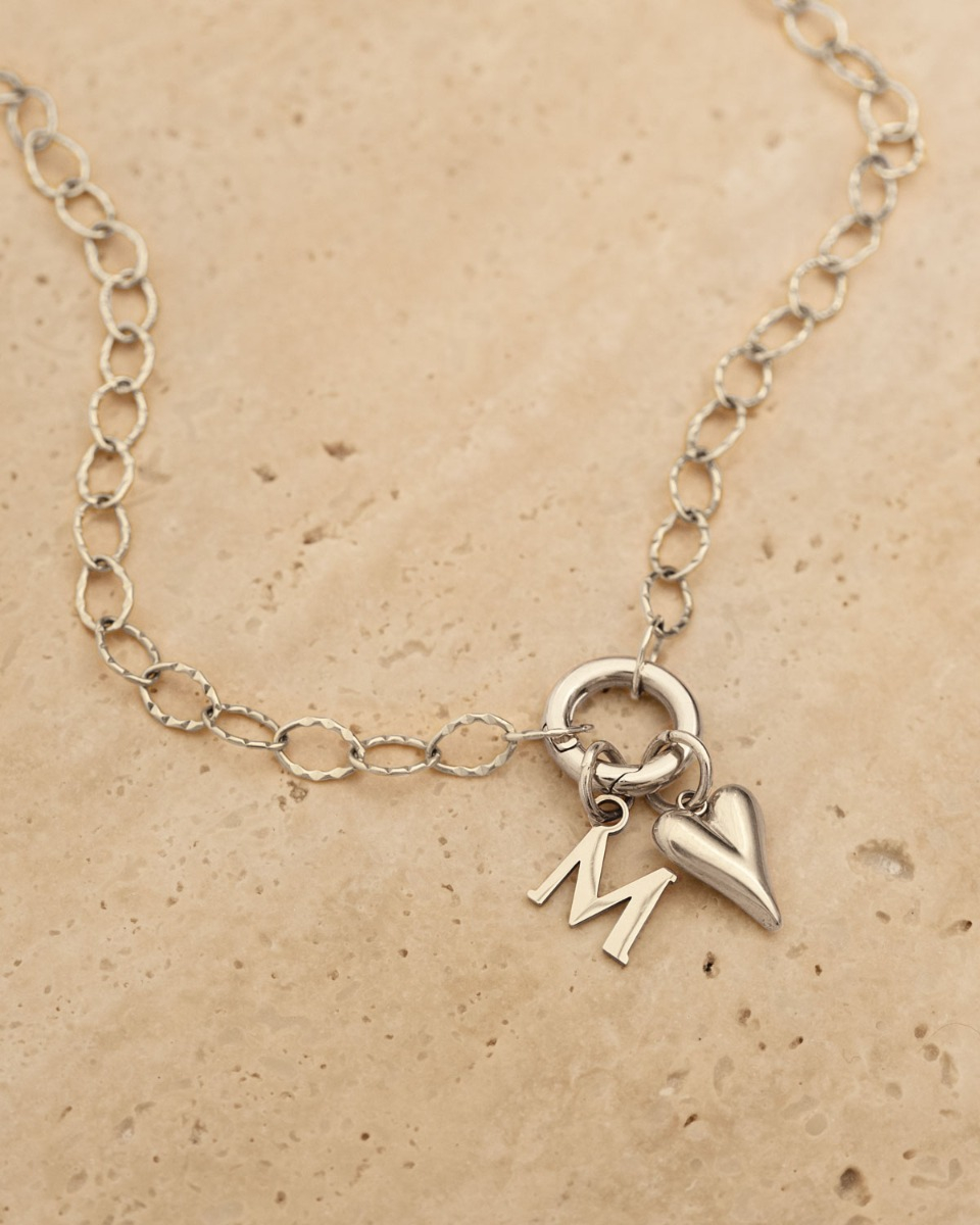 zilveren initial ketting met hartjes bedel op beige stenen ondergrond