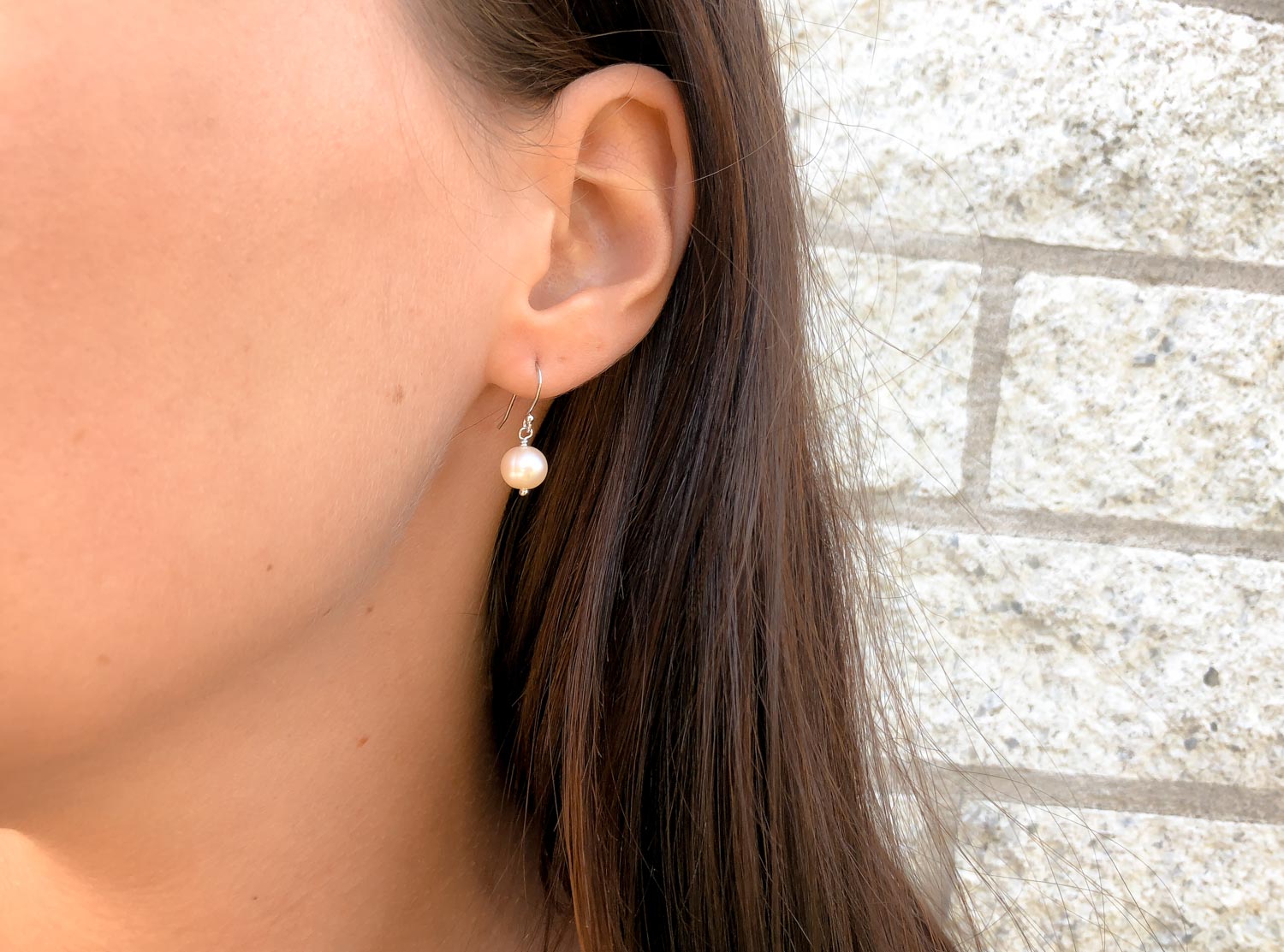 Vrouw draagt zilveren oorbel met peach parel van DRKS