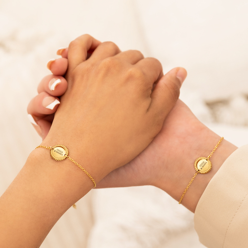 Een moeder en dochter hand die elkaar vast houden. Ze hebben dezelfde armband om. het is een goud fijn armbandje met een vintage rondje als bedel. Op de bedel staat Tessa en mama gegraveerd