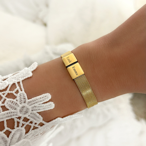 Gouden armband om pols met kanten blouse aan. Met 2 bedeltjes, op de bedeltjes staan namen gegraveerd