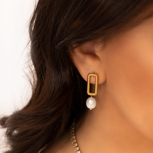 Gouden parel oorbellen in oor van meisje met bruin haar